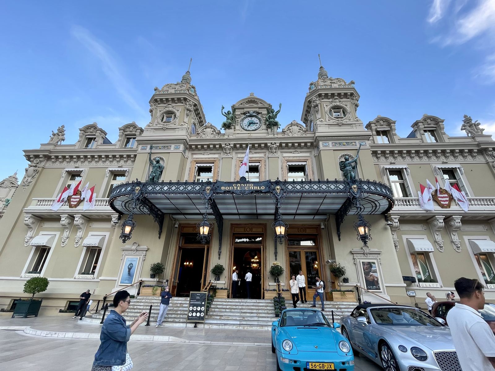 The Monte-Carlo Casino — ornate Belle Époque facade, blue sky, Ferraris and Bentleys parked outside